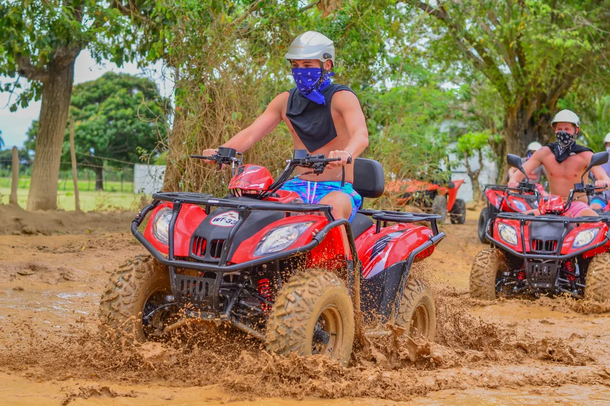 Travelers riding red ATVs through muddy countryside trails during a Punta Cana road adventure